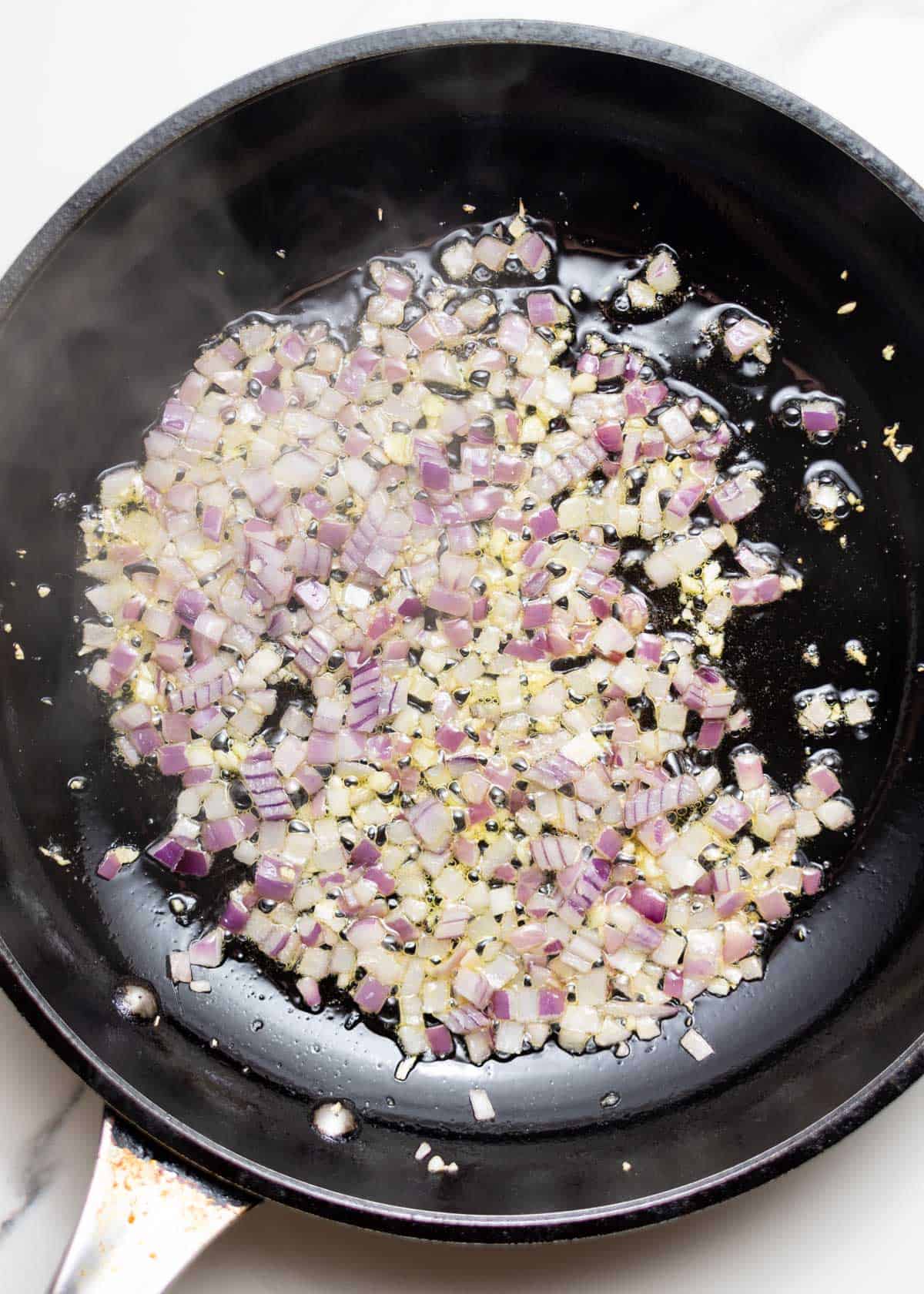 Diced onion and minced garlic sautéing in a skillet.