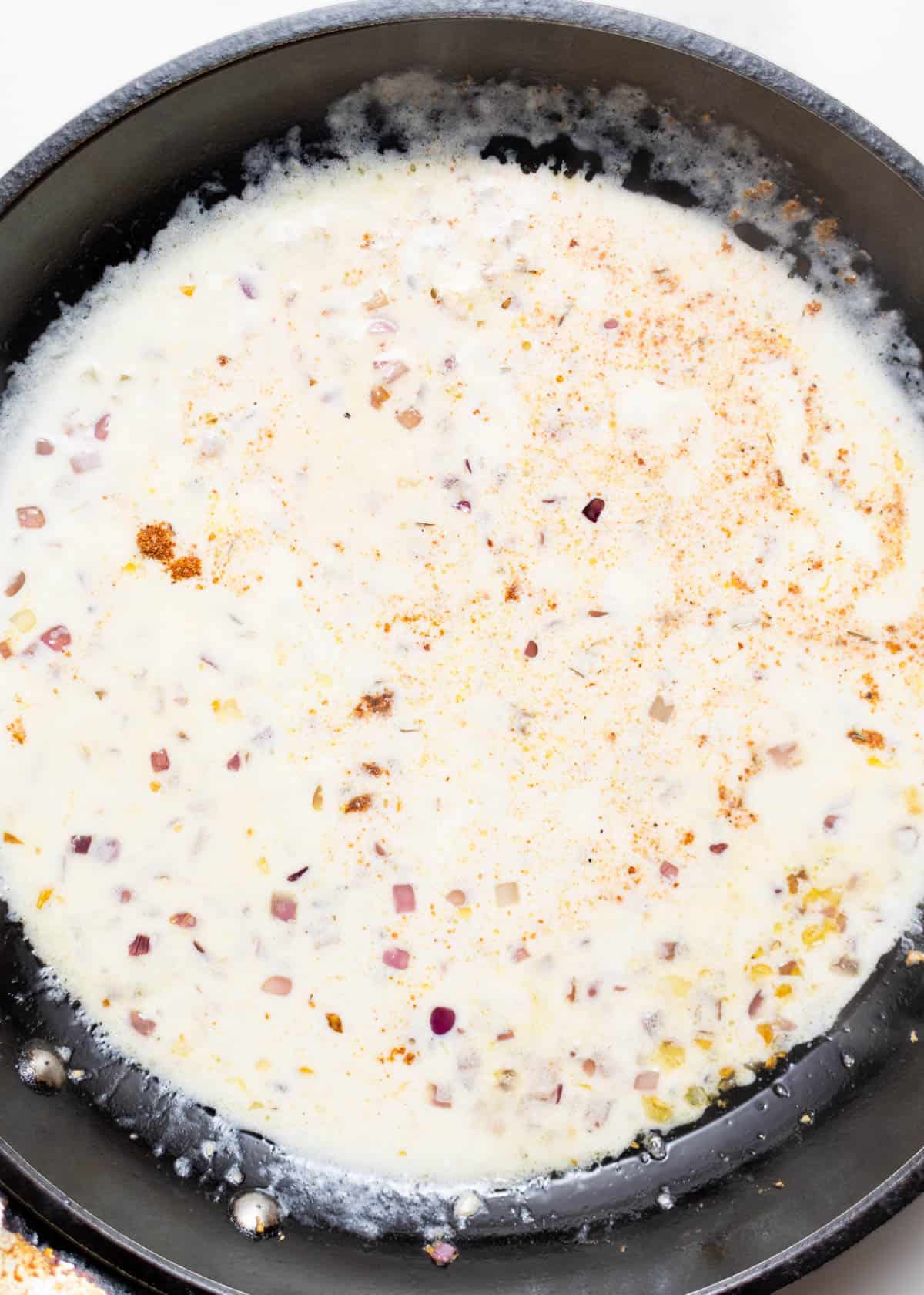 Pouring heavy cream over sautéed diced onion and minced garlic.