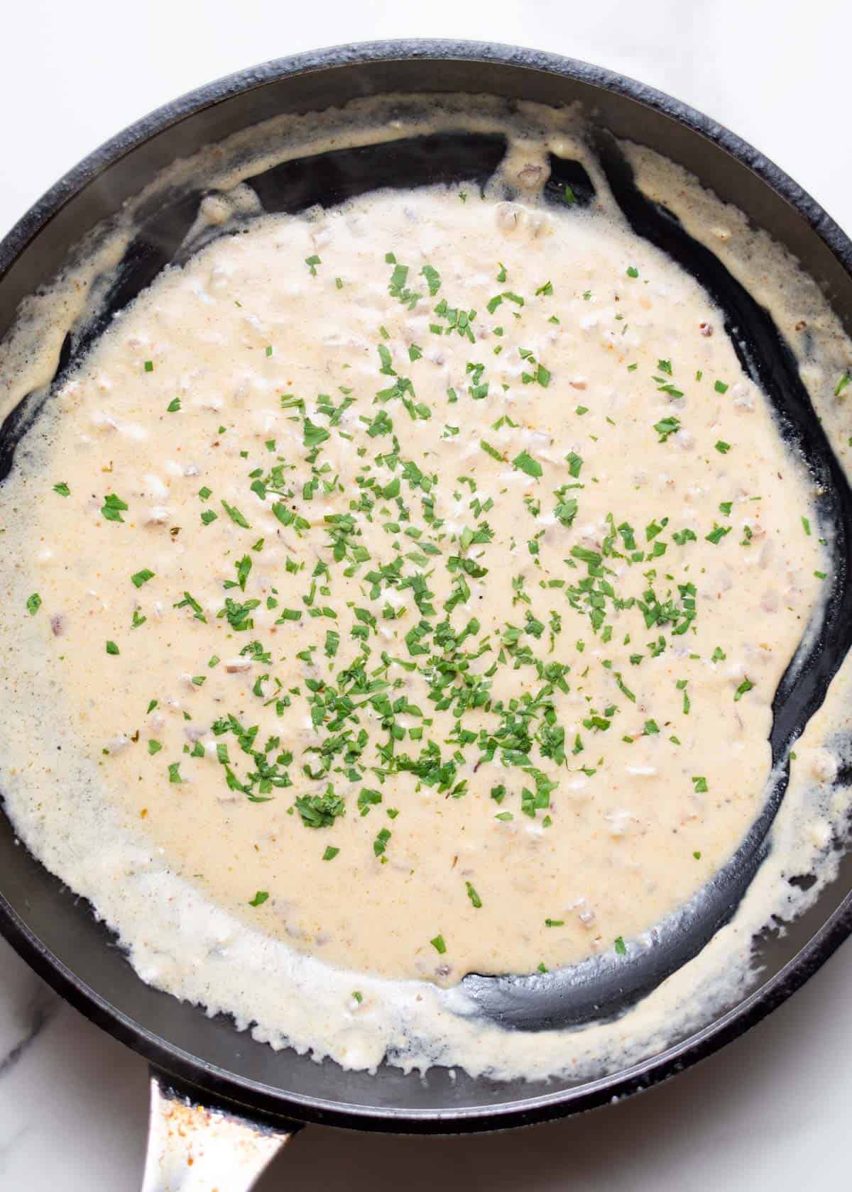 Cajun Alfredo sauce in skillet with heavy cream and chopped parsley on top.