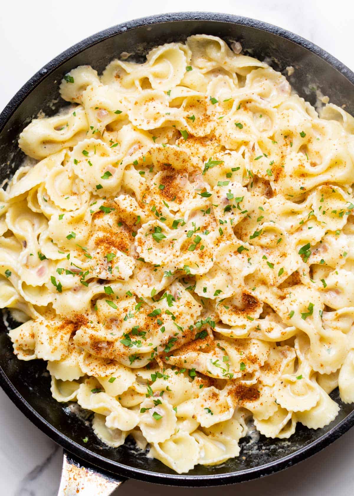 Cajun farfalle Alfredo with chopped parsley on top in a skillet.