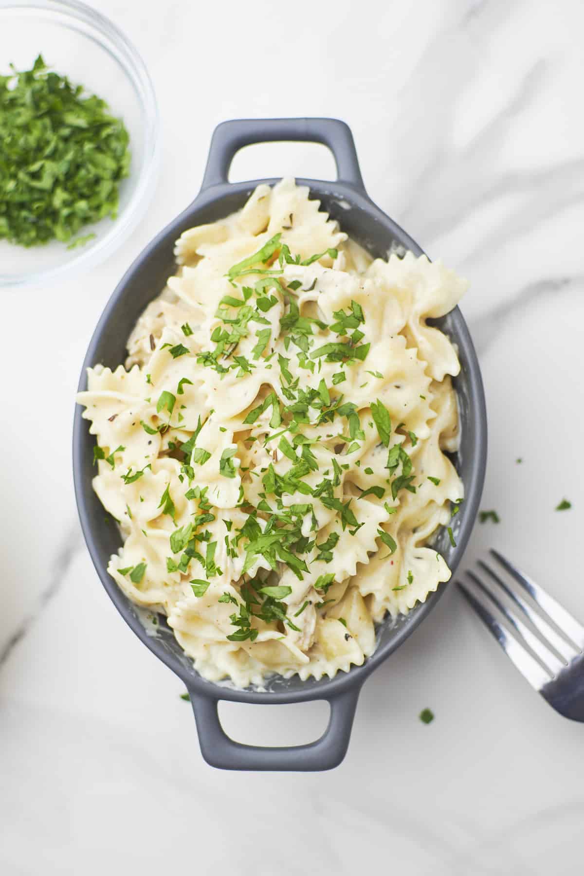 bowl of garlic parmesan chicken pasta with parsley sprinkled on top and fork to the side.