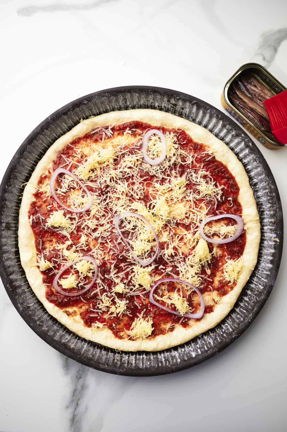 pizza dough with red sauce, cheese and red onions.