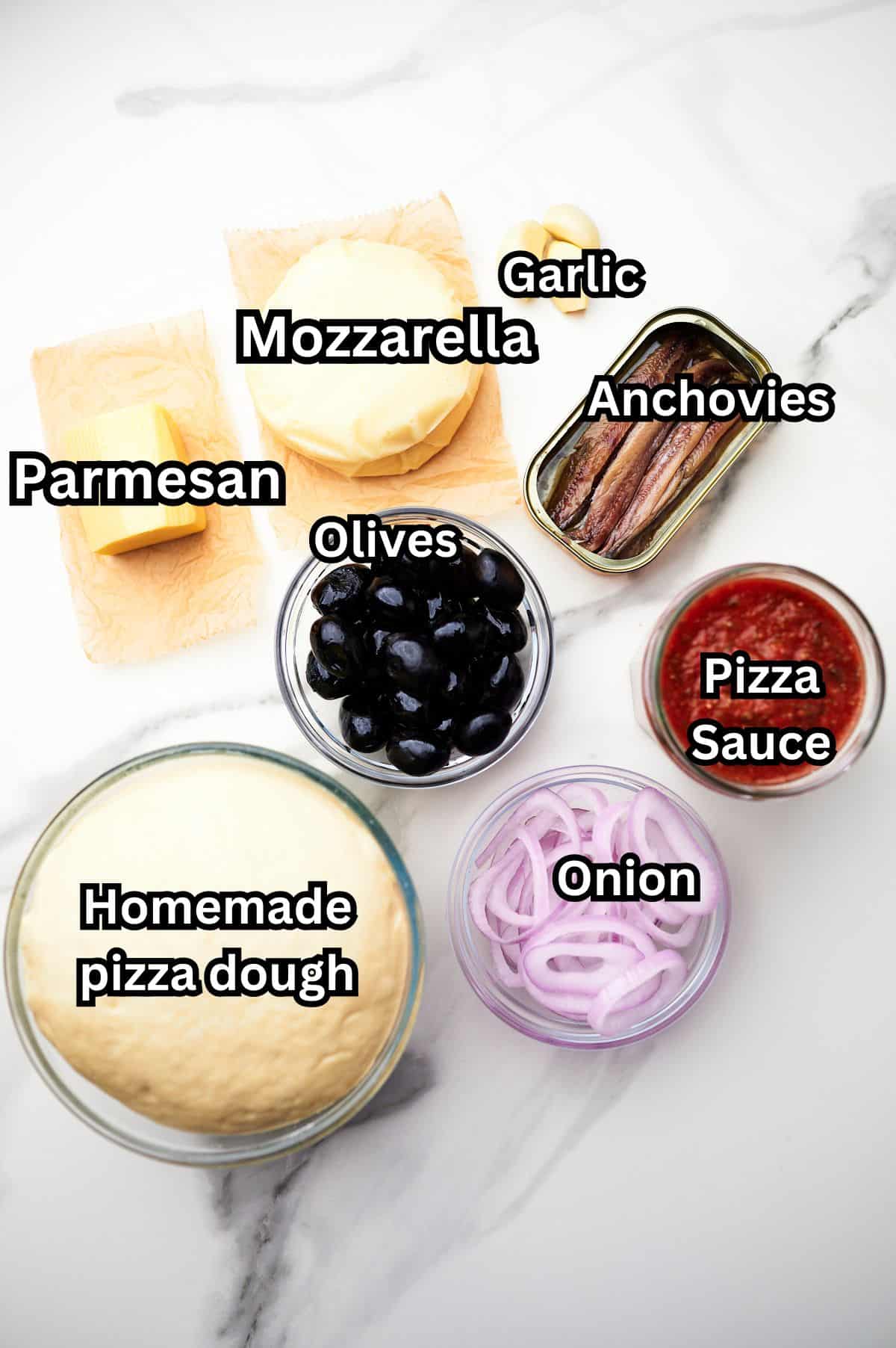 ingredients for anchovy pizza on countertop, labeled.