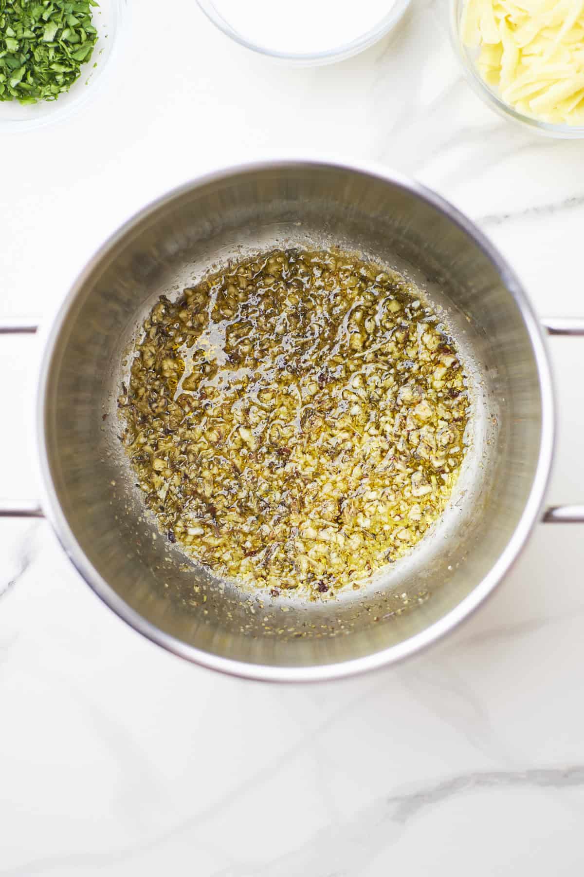 Large white sauté pan filled with sautéed garlic and dried herbs.