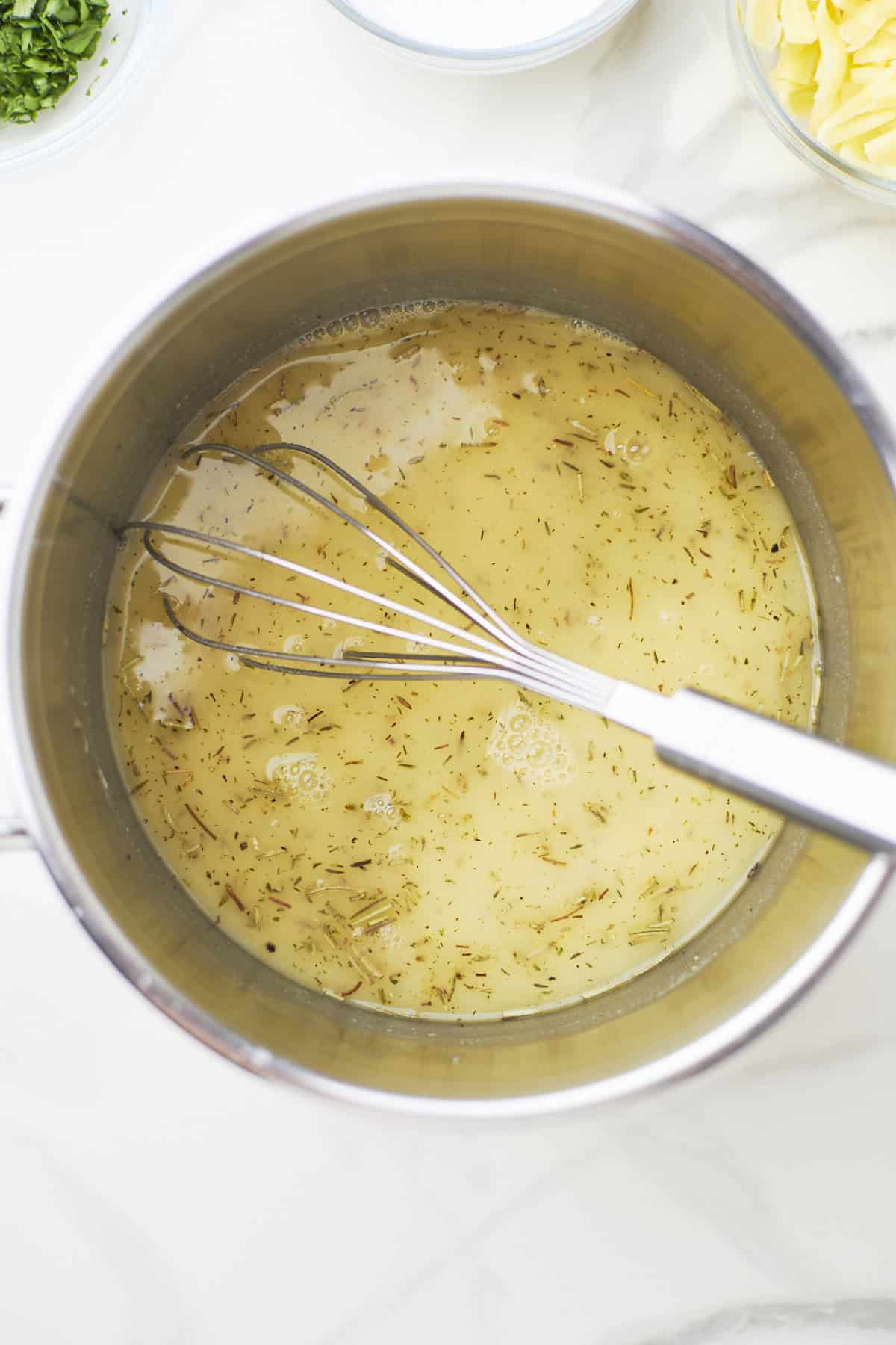 Large white sauté pan filled with sautéed garlic dried herbs and flour.