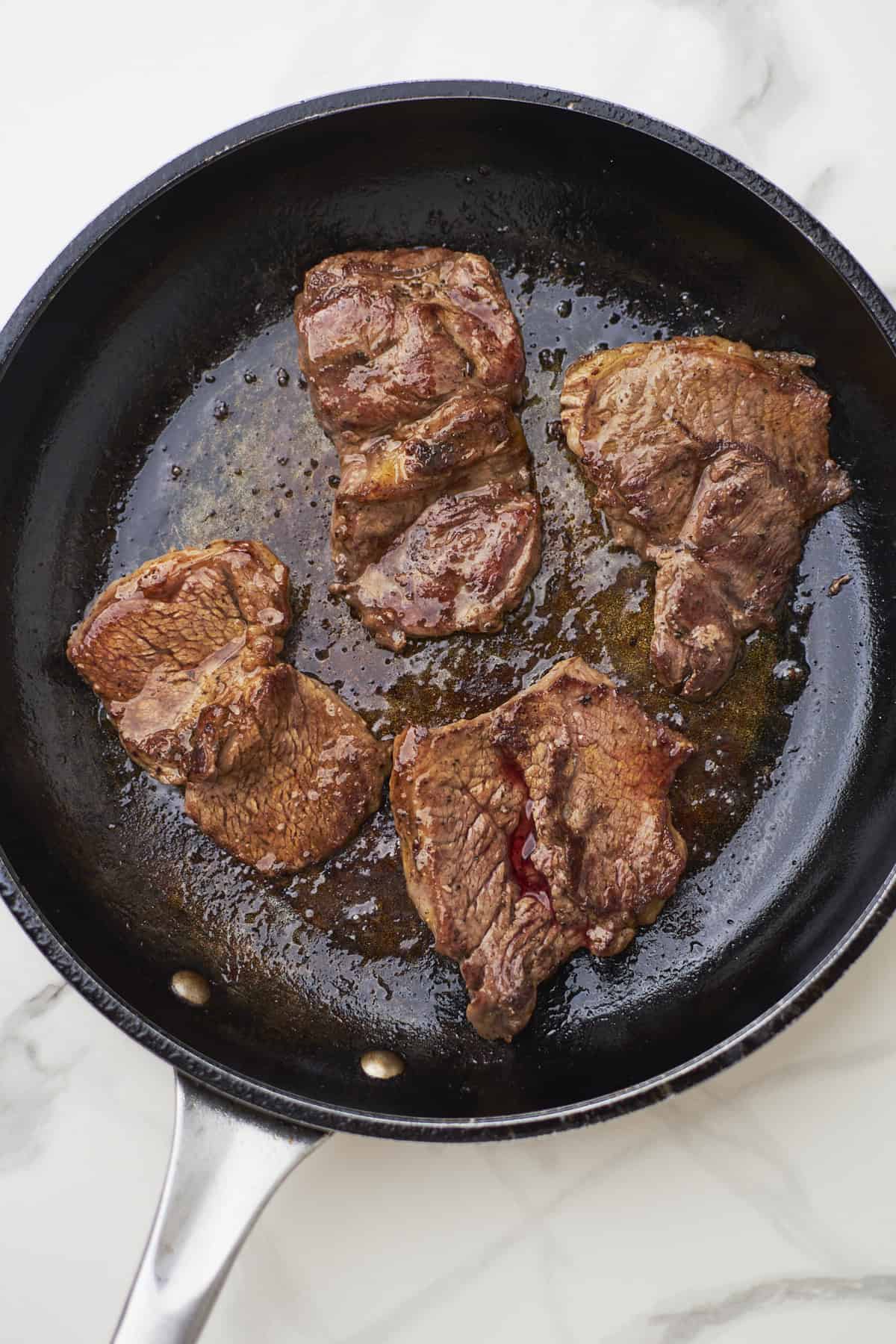 Steak cooking in a skillet.