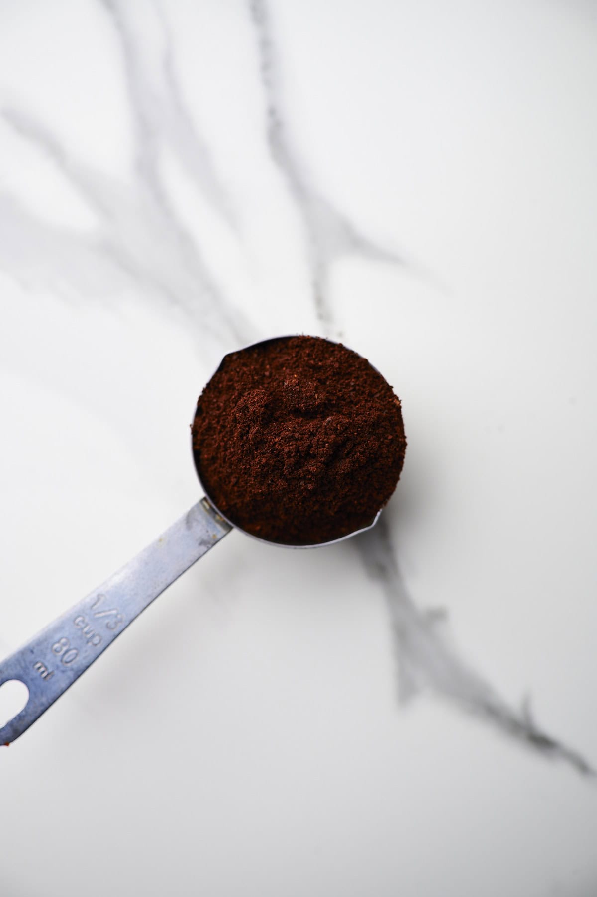 ground coffee beans in measuring cup on counter-top.