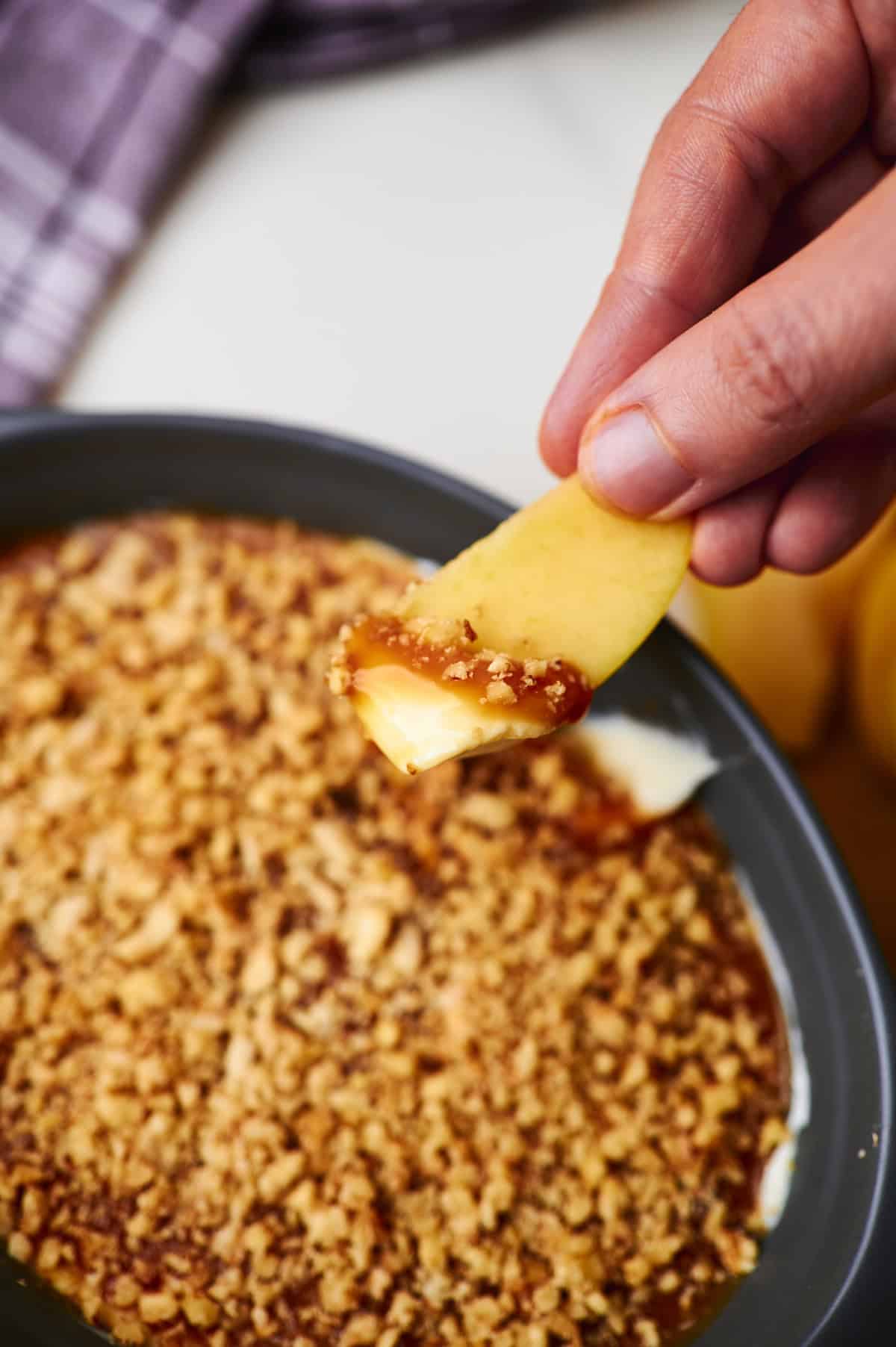 an apple being dipped in a caramel, cream cheese, and toffee bit dip