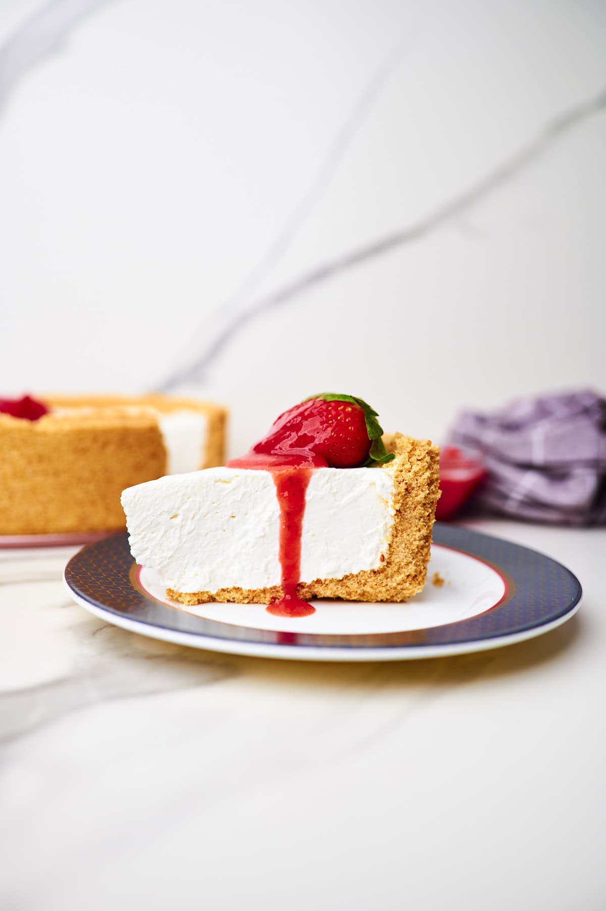 slice of no bake cheesecake with cool whip in graham cracker crust topped with strawberry pie filling on plate