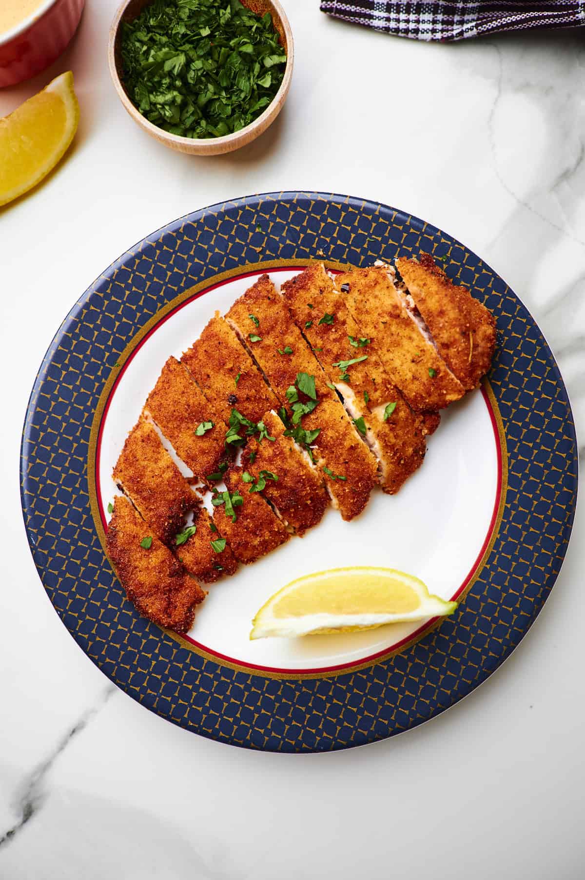 Crispy Panko chicken sliced on a white plate garnished with parsley and lemon wedges.