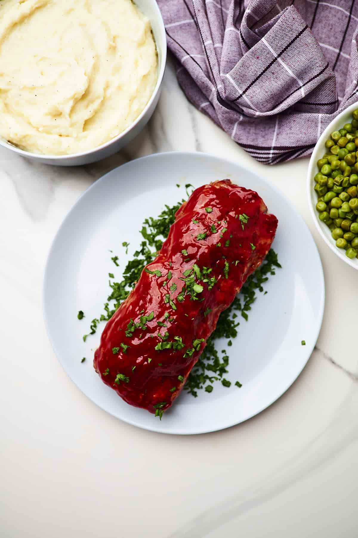 meatloaf with stuffing on a platter with parsley, mashed potatoes and peas.