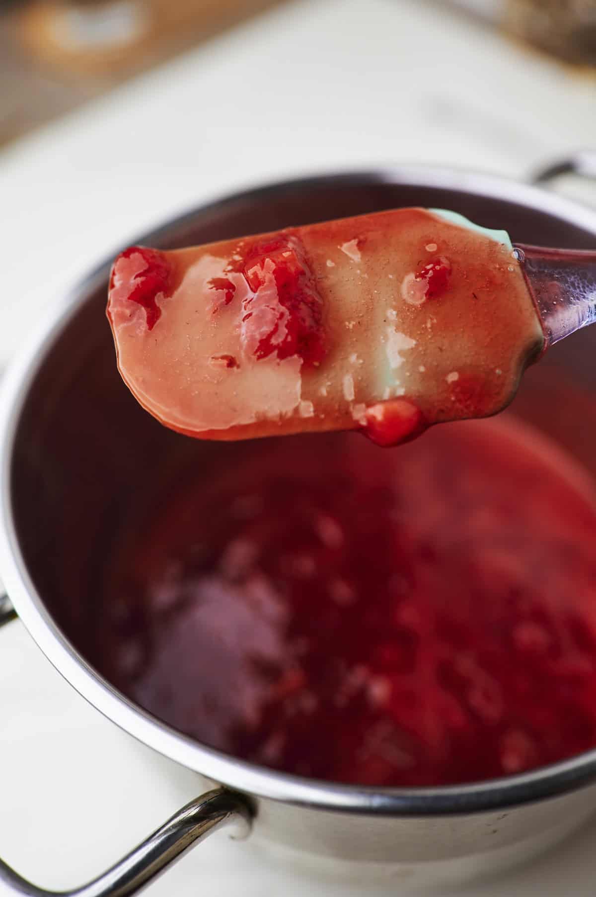 strawberry sauce thickening in saucepan, clinging to the back of a spatula.