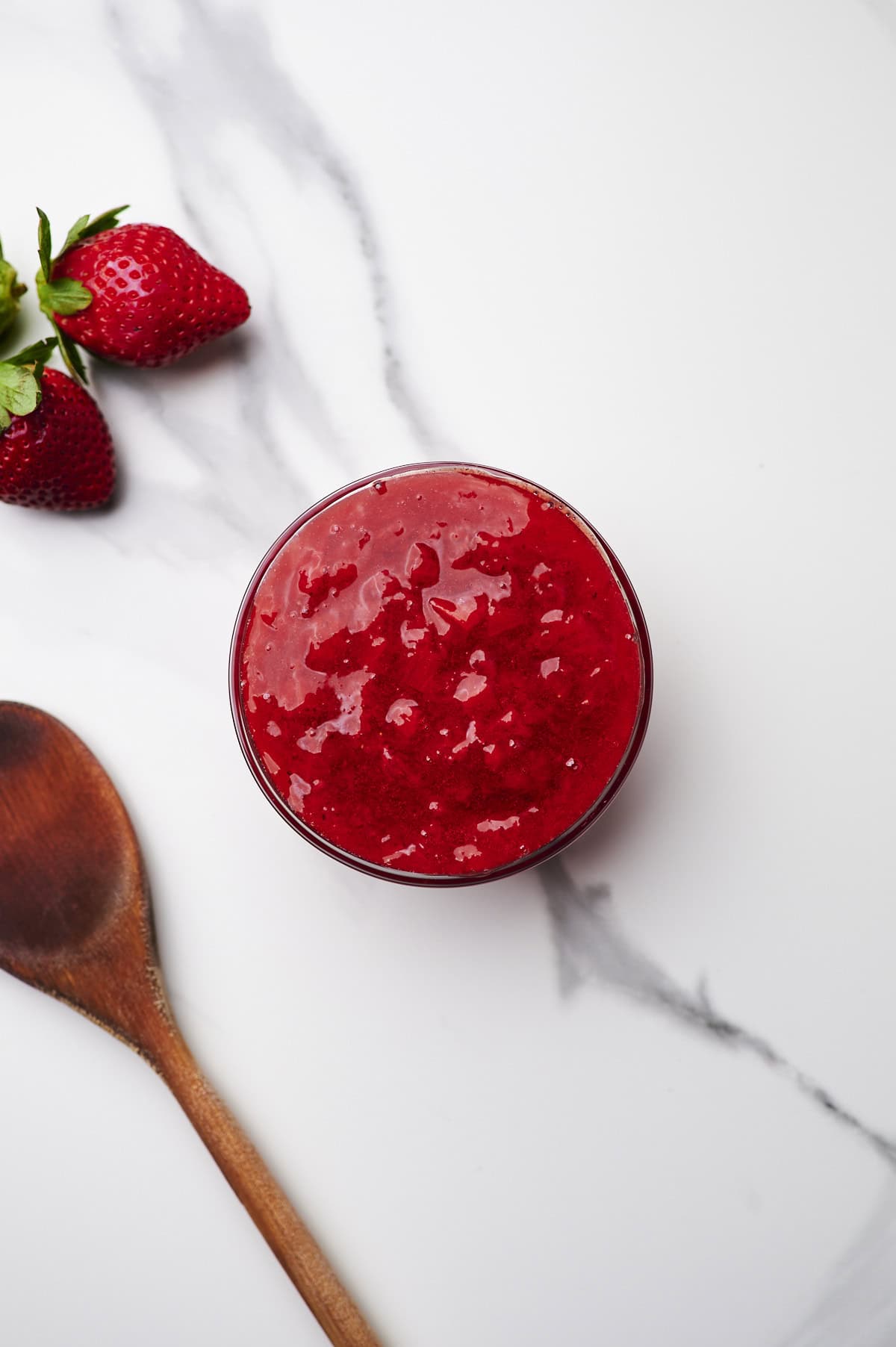 strawberry filling for cakes in bowl on countertop with wooden spoon to the side.