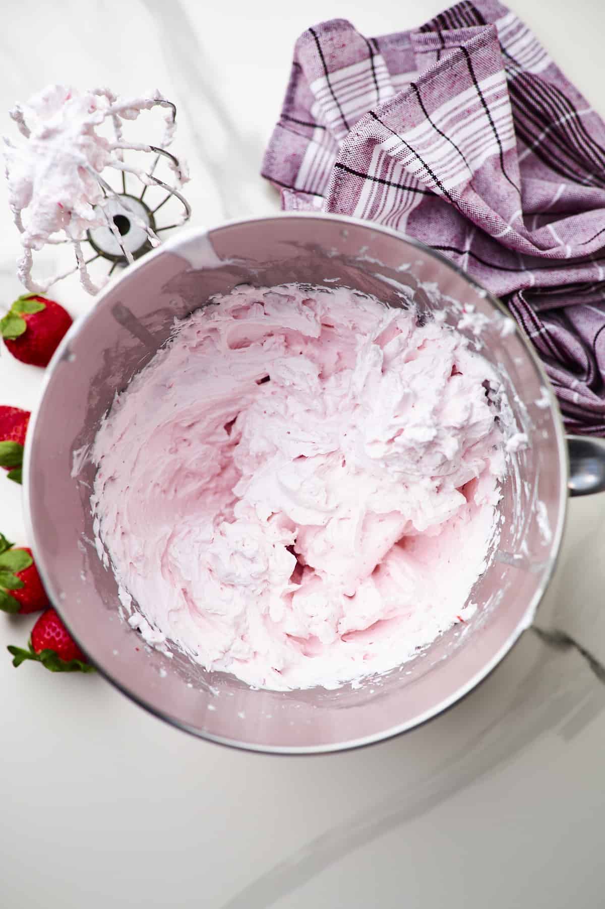 closeup of strawberry whipped cream frosting with whipping hook on the side.