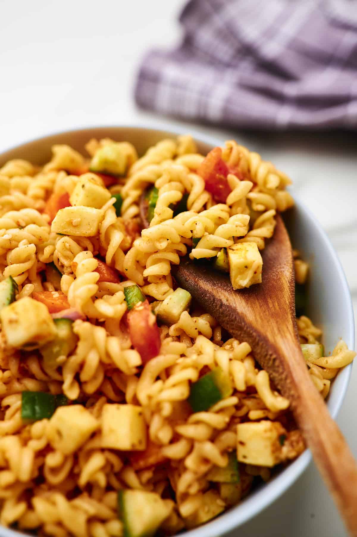 supreme pasta salad with a wooden spoon taking a spoonful