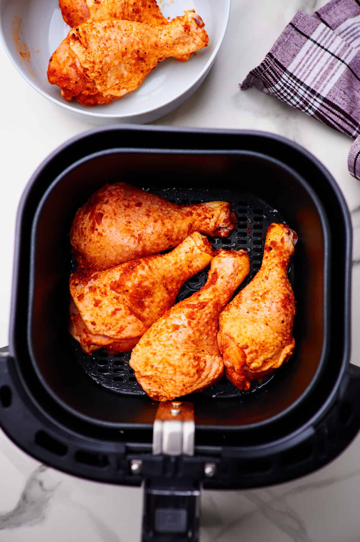 Seasoned chicken drumsticks in the air fryer basket before being cooked. 