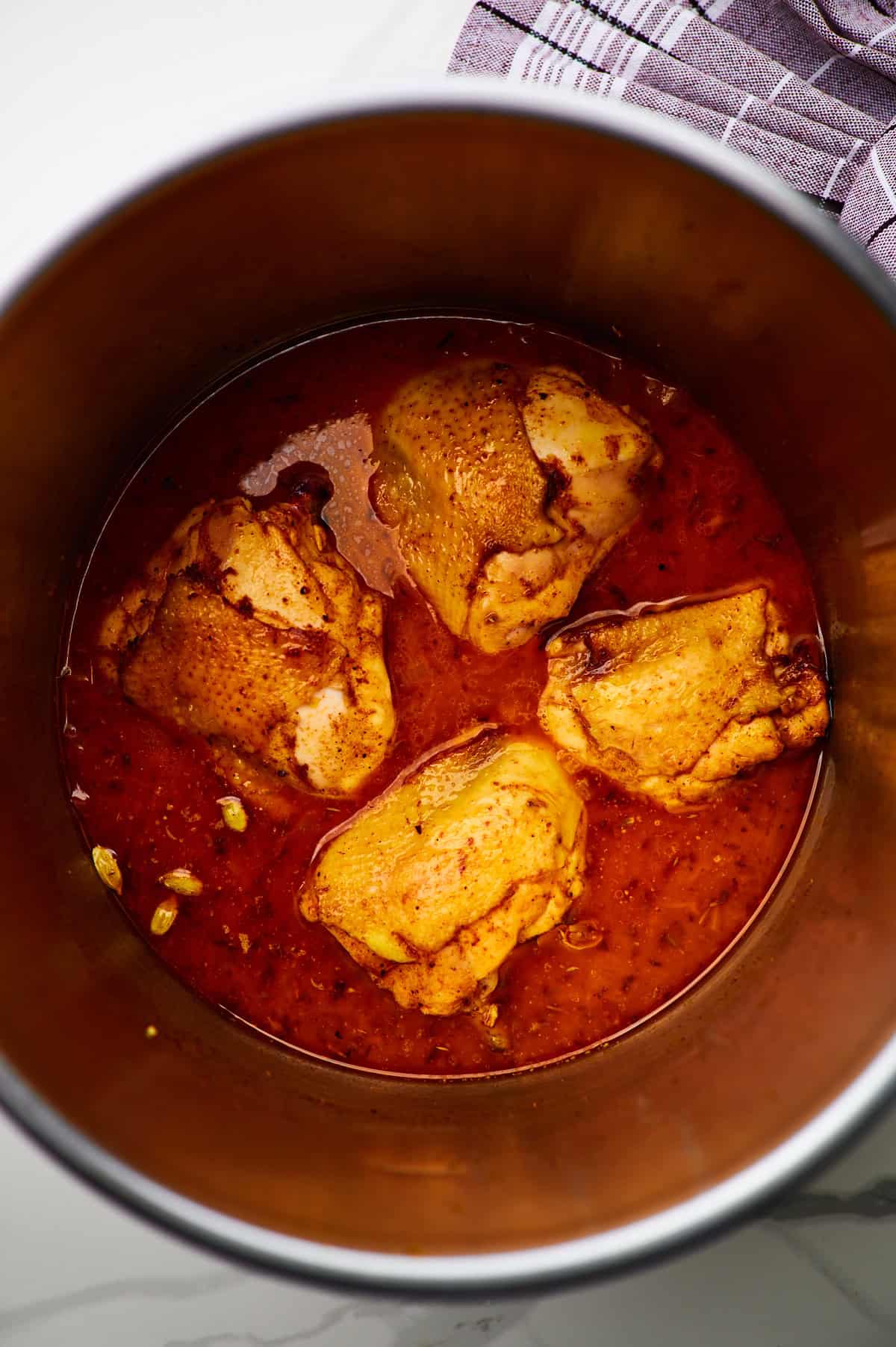 seared chicken thighs and yellow rice simmering in broth in a pan on the stovetop.