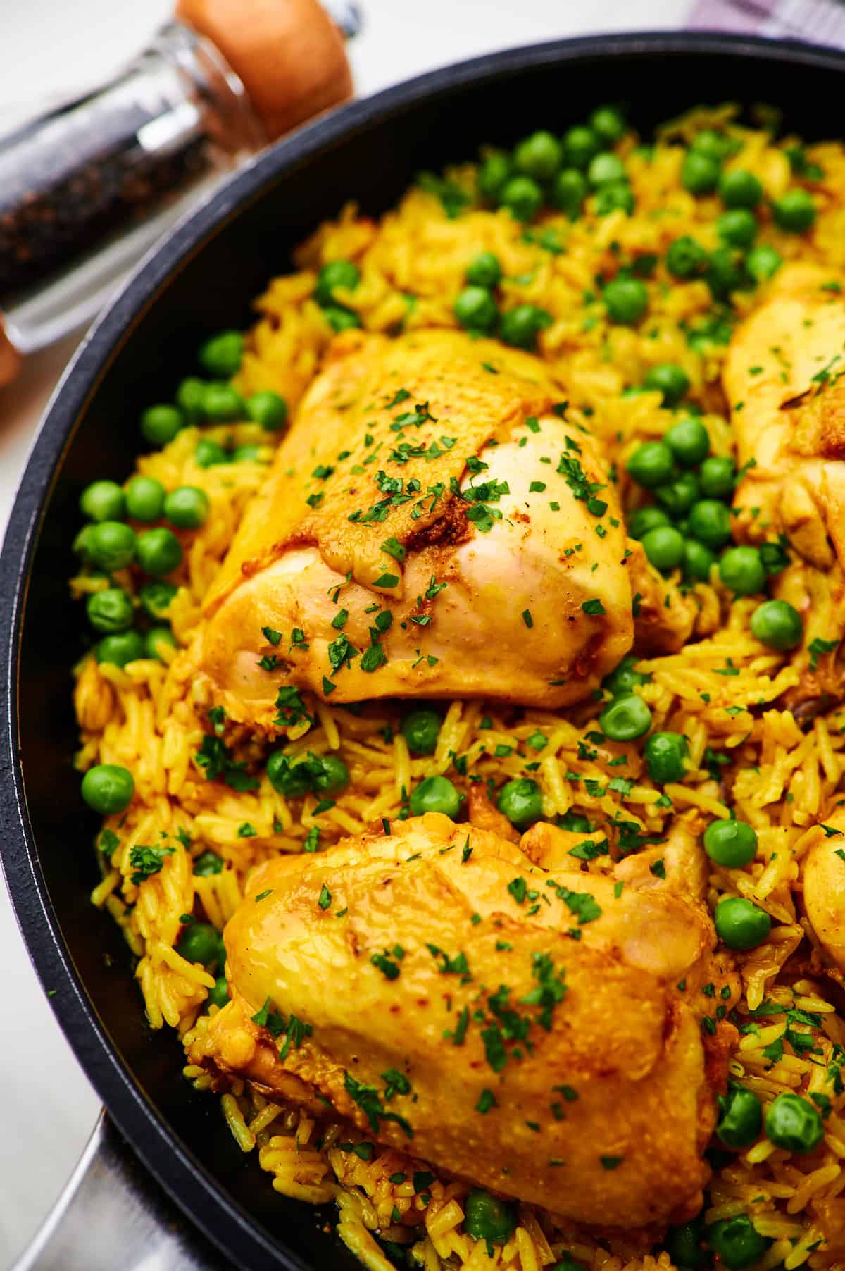 chicken and yellow rice with peas in a pan on a table with pepper in the background.