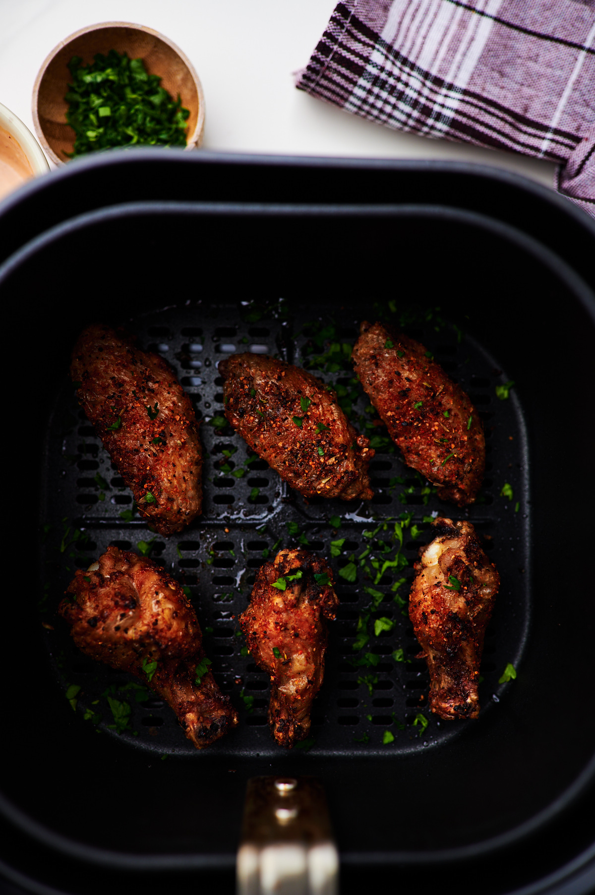 Chicken wings in the air fryer basket garnished with fresh parsley.