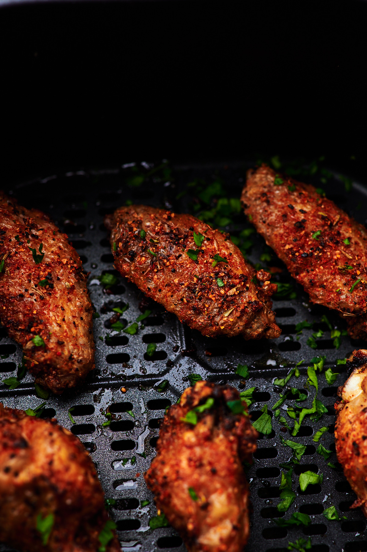 Air Fryer Chicken wings in the basket of the air fryer and garnished with fresh parsley. 