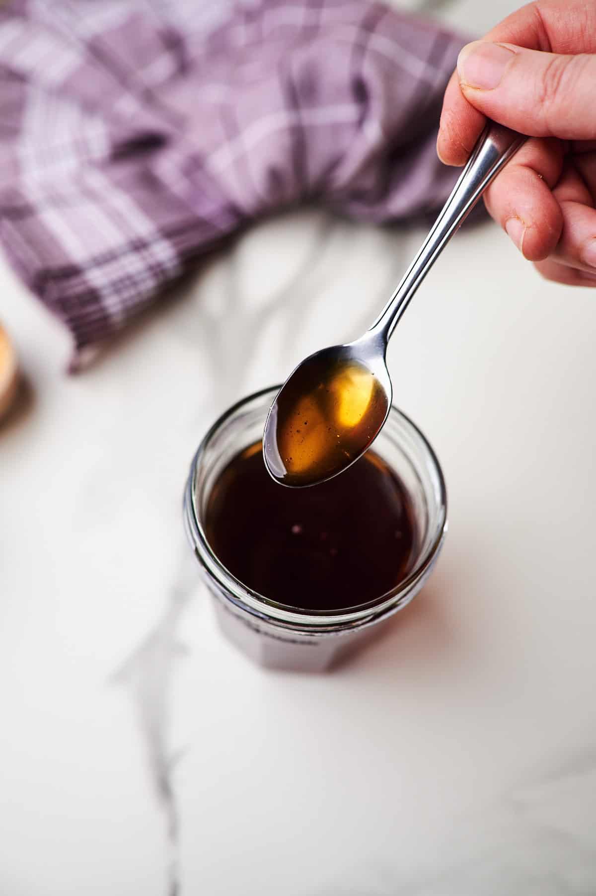 A spoon dripping brown sugar simple syrup into a mason jar.