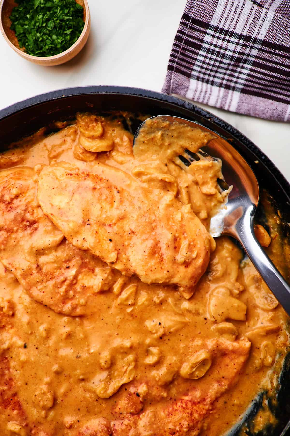 Creamy mushroom sauce chicken in a skillet with a spatula for serving.