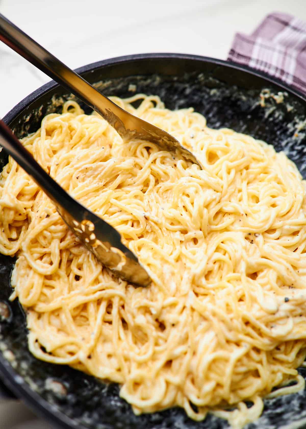 a skillet with creamy garlic pasta and kitchen tongs