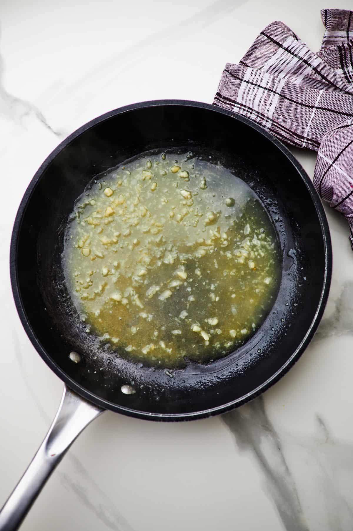 making a roux in a skillet and stirring in ingredients for creamy garlic sauce