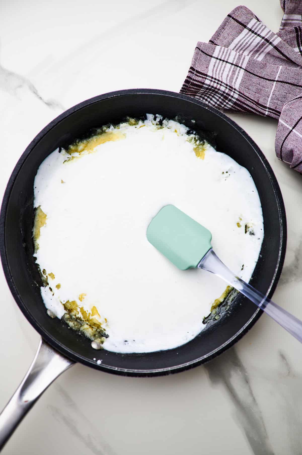 making a roux in a skillet and stirring in ingredients for creamy garlic sauce