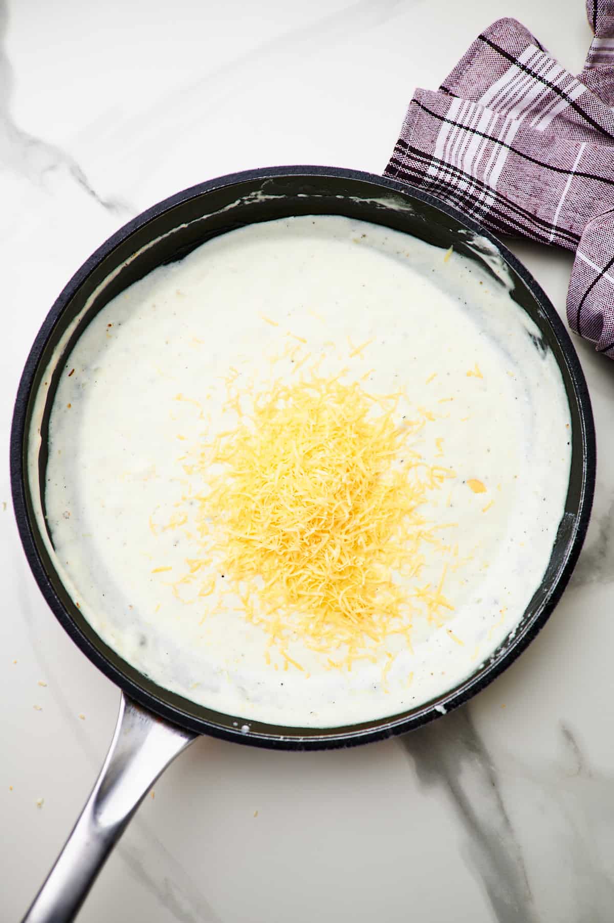 adding parmesan to a skillet and tossing pasta with creamy garlic sauce