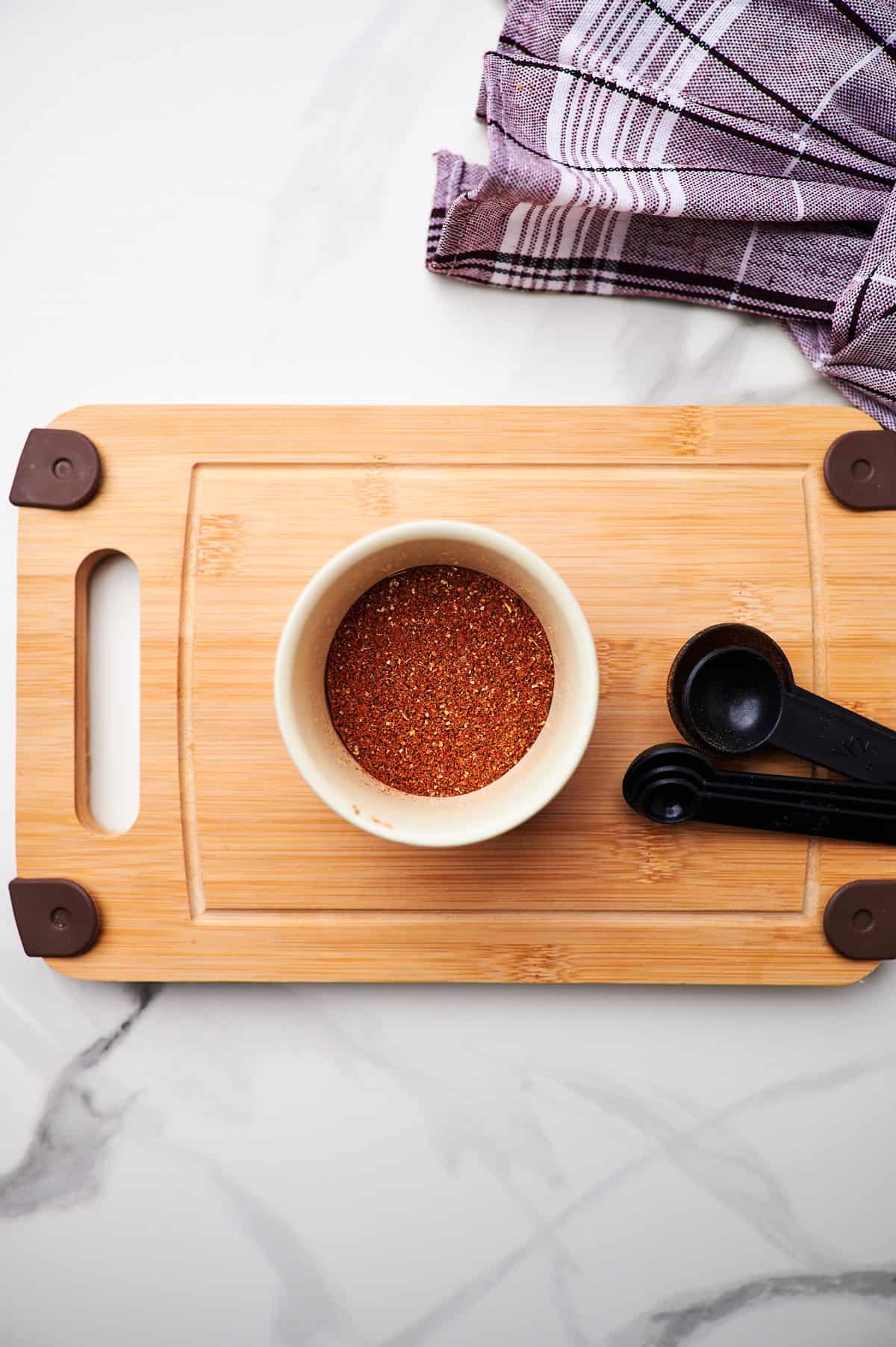 A white bowl of ground turkey taco seasoning with a measuring spoon on a wooden board.