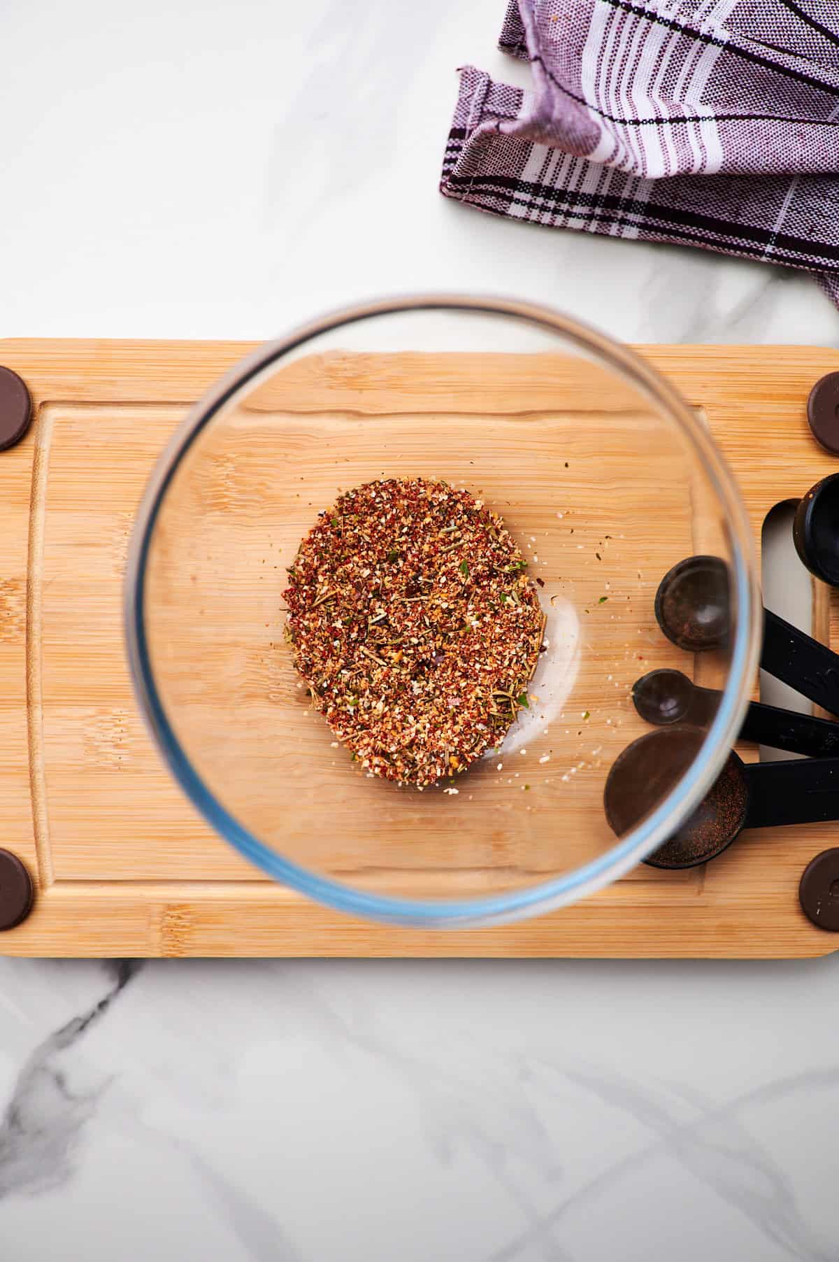 A glass bowl full of ground turkey seasoning with a measuring spoon.