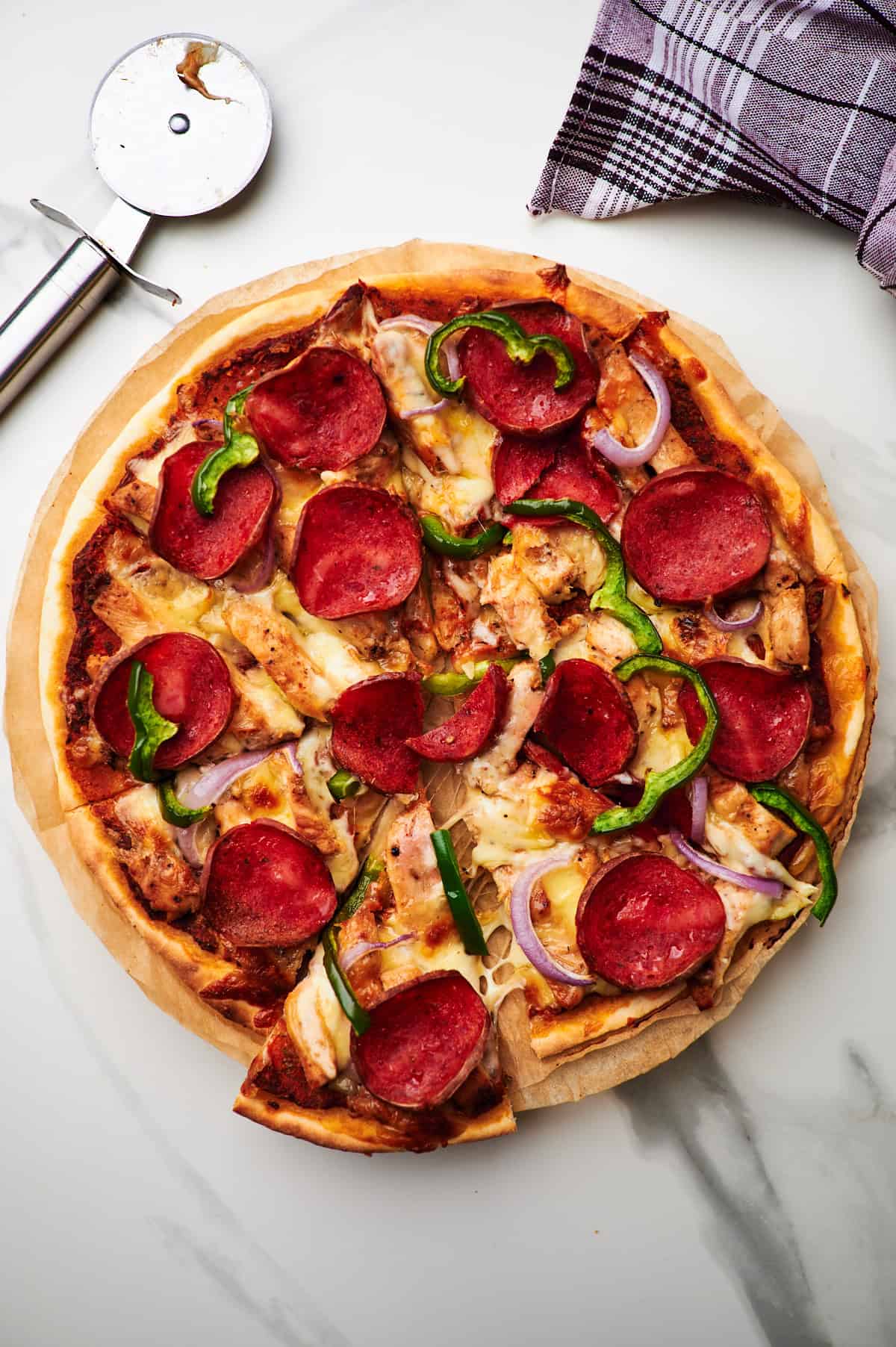 High protein pizza with two slices cut on a white plate on a countertop.