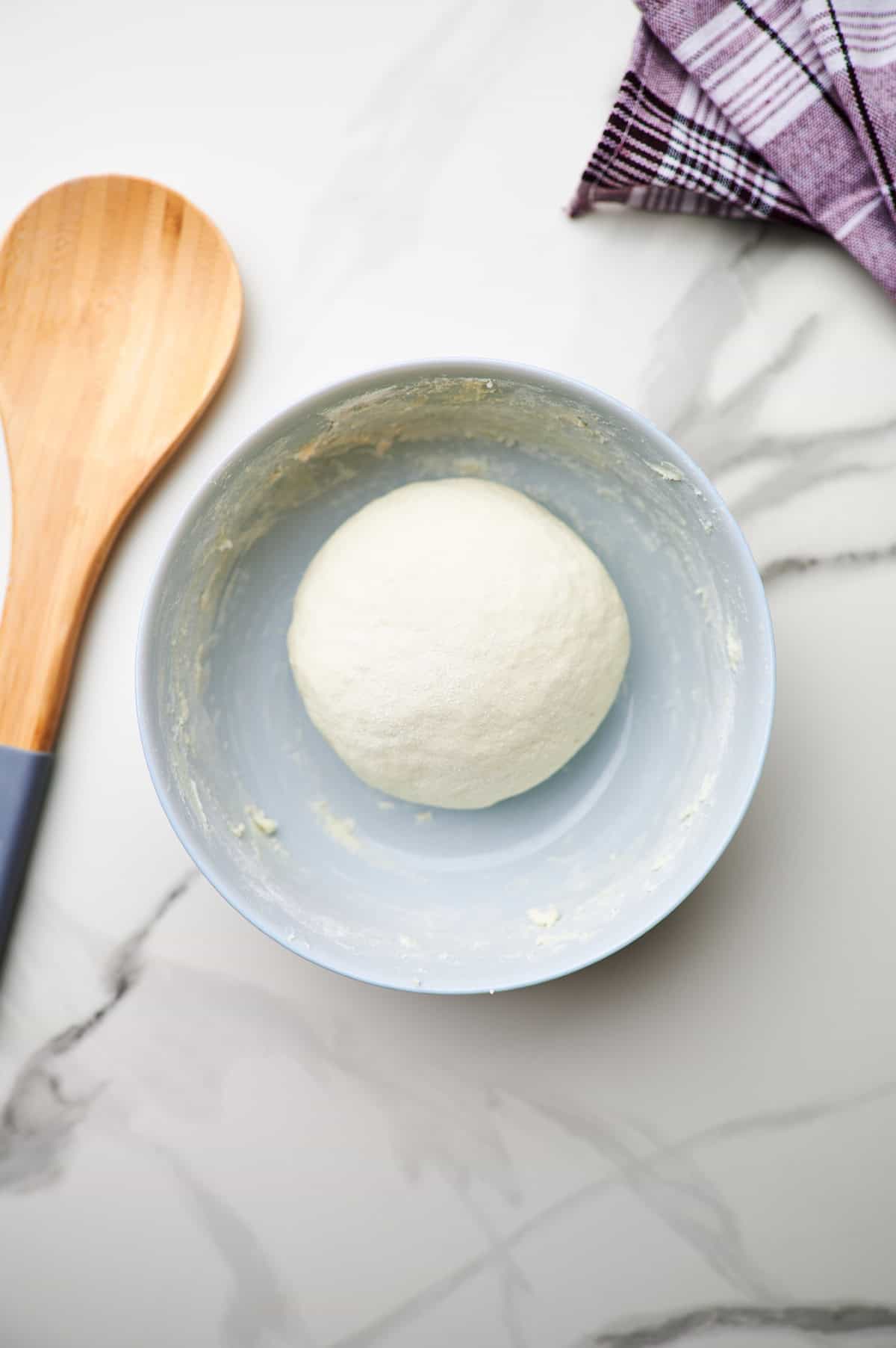 High protein pizza dough in a white bowl on a countertop.