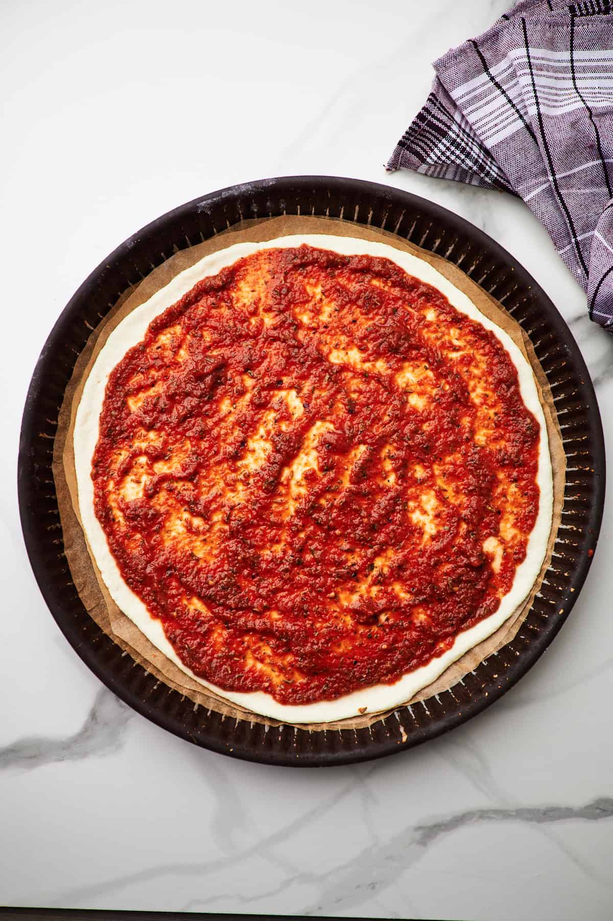 Tomato sauce on pizza dough on parchment paper.