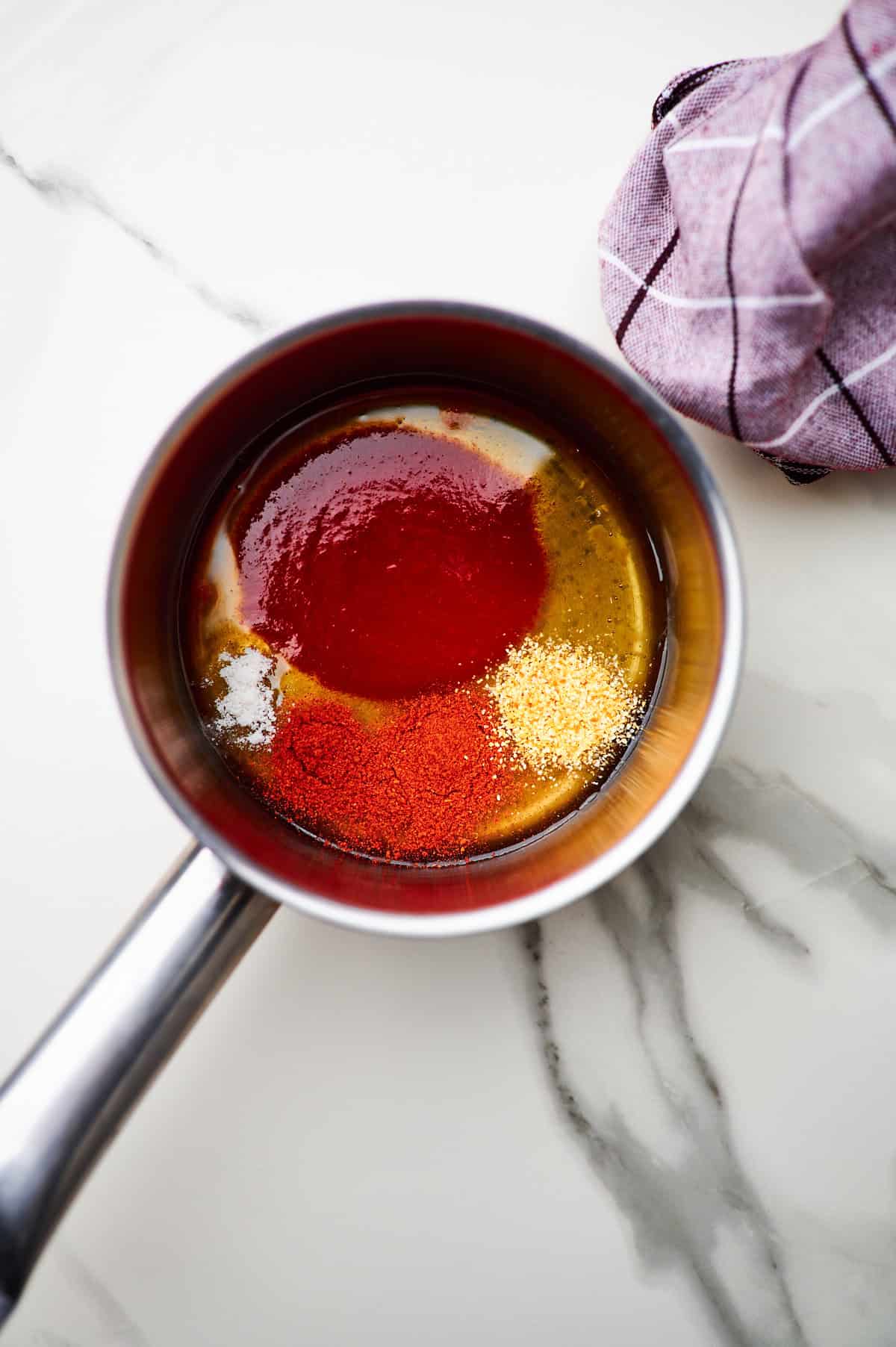 honey, hot sauce, and seasonings added to a small silver saucepan to make the spicy hot honey sauce.