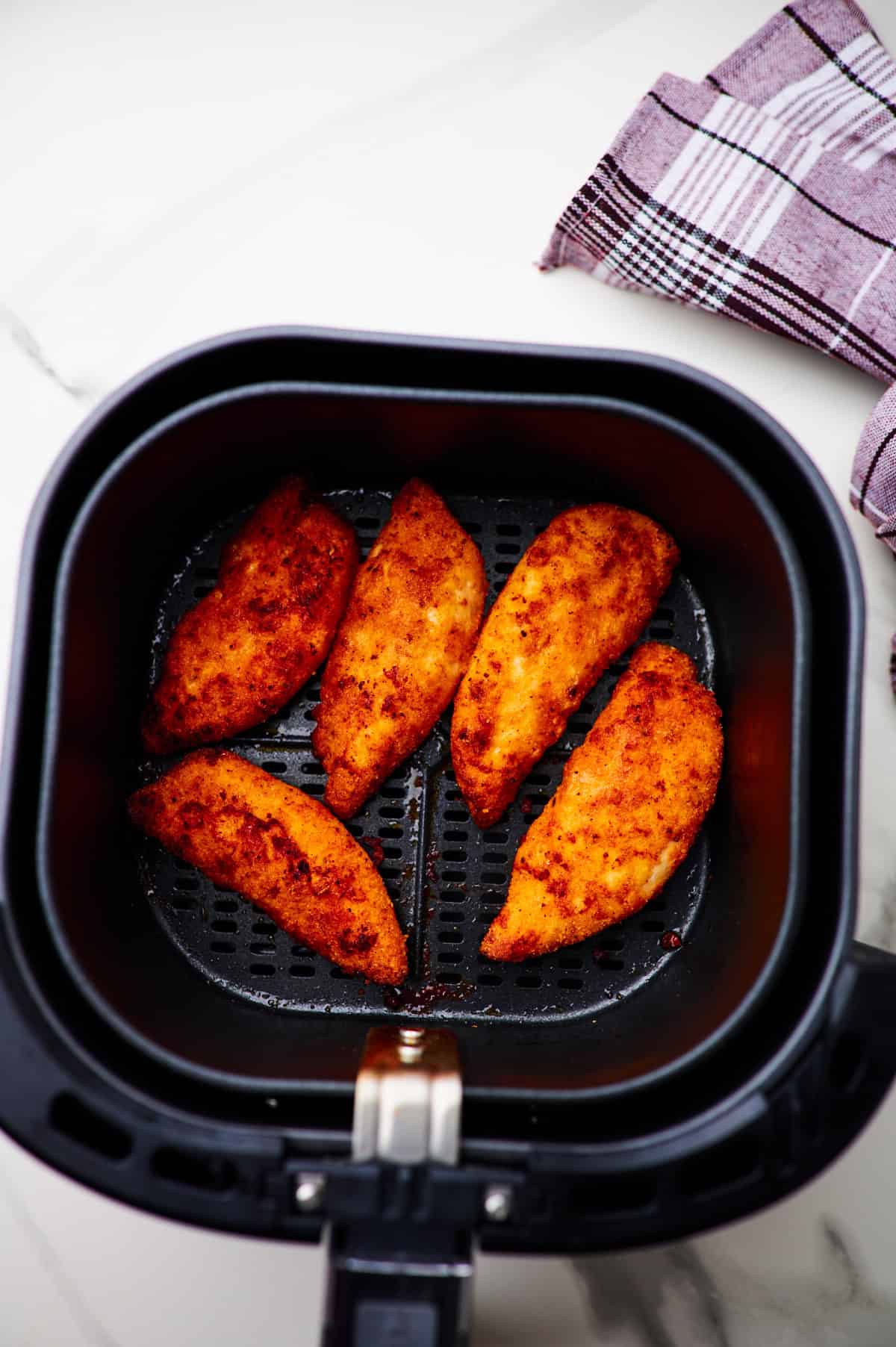 5 homemade spicy chicken tenders in the base of an air fryer.