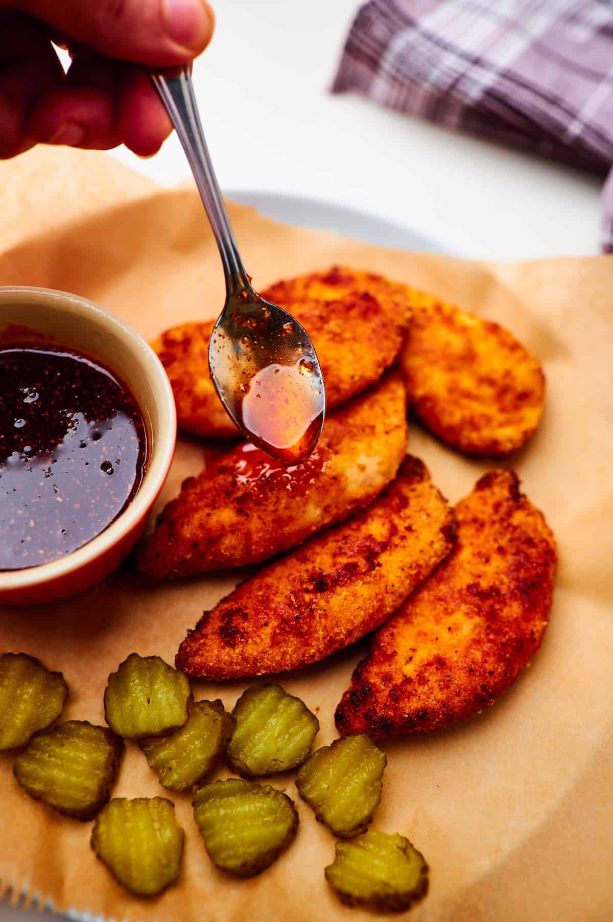 action shot of homemade hot honey sauce being drizzled over spicy air fryer chicken tenders on a white plate.