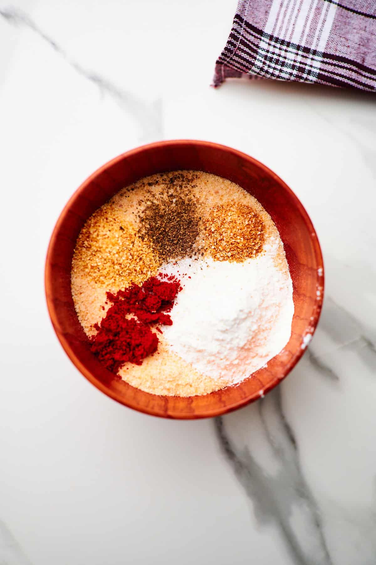 breadcrumbs, flour, and seasonings added to a bowl to make the chicken breading mixture before stirring together.