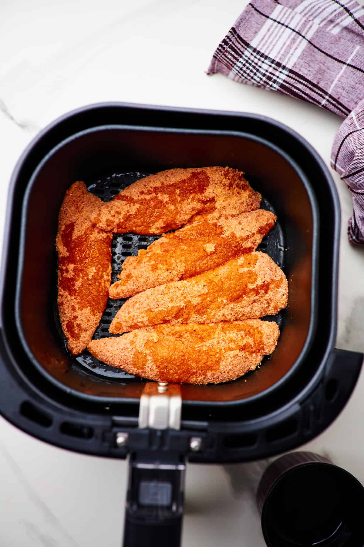 5 raw breaded chicken tenders in the base of an air fryer.