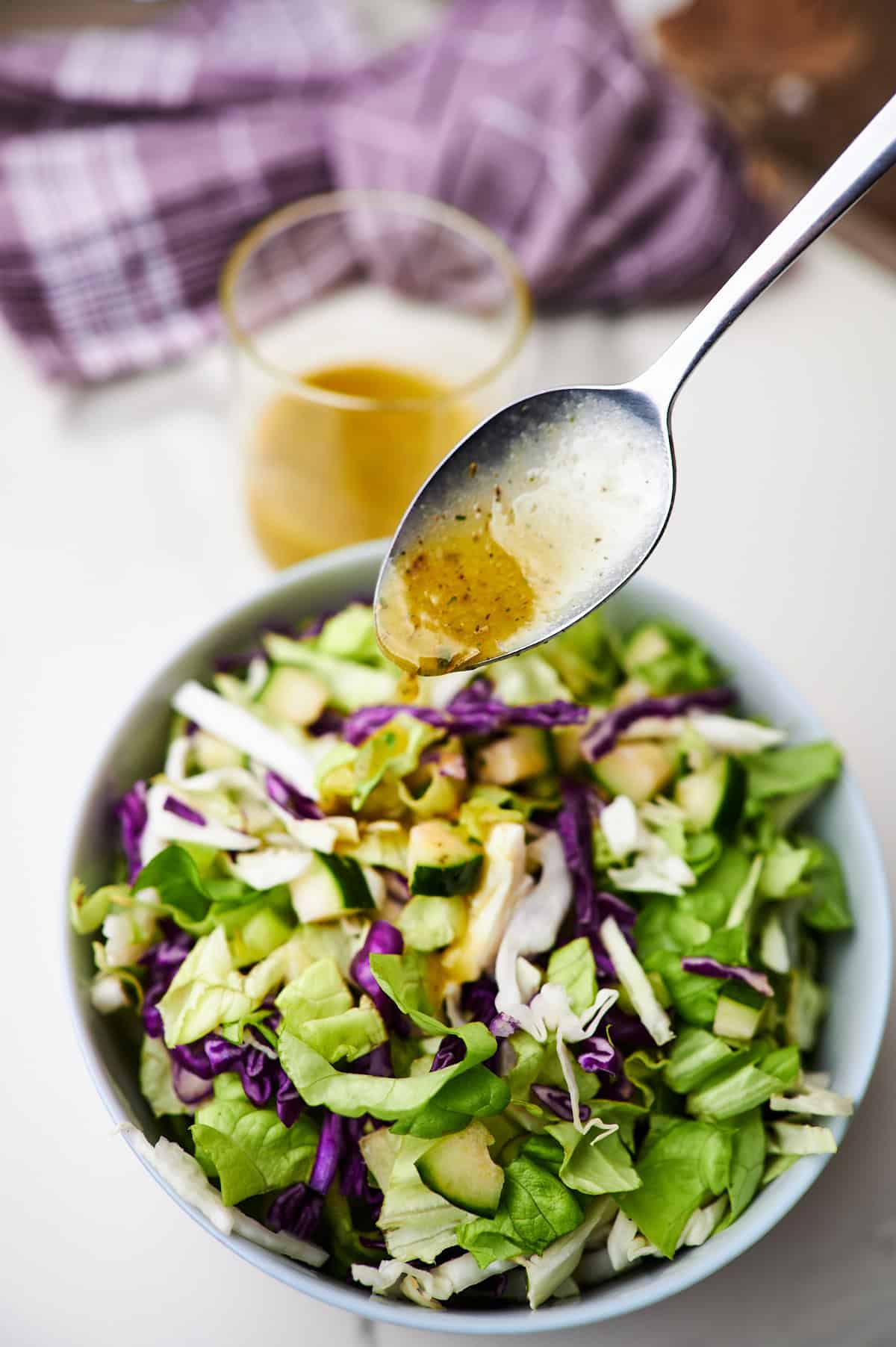 A spoonful of salad dressing being put into an italian sub sandwich.