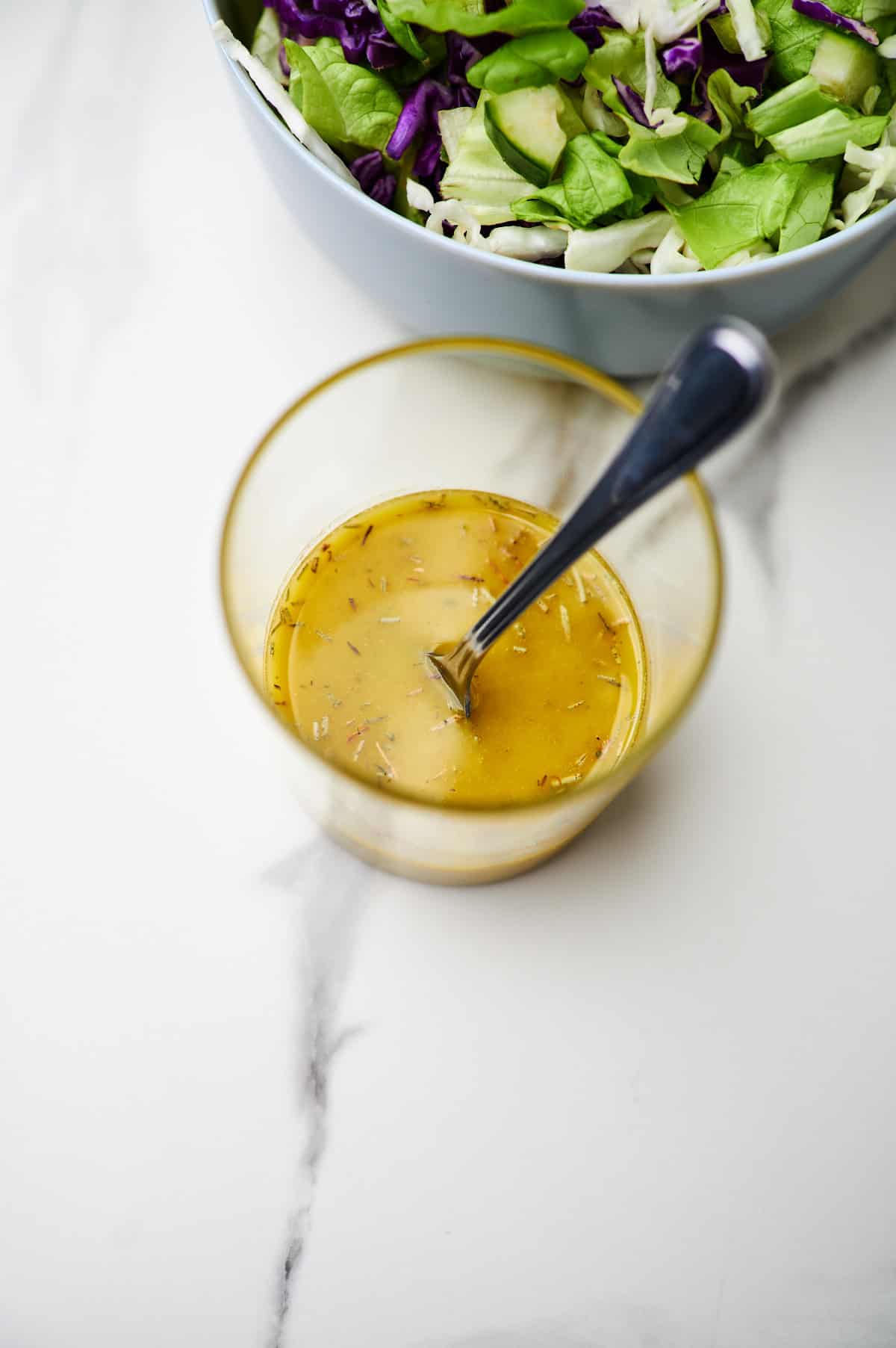 A small glass jar of italian submarine dressing with a spoon and a salad.