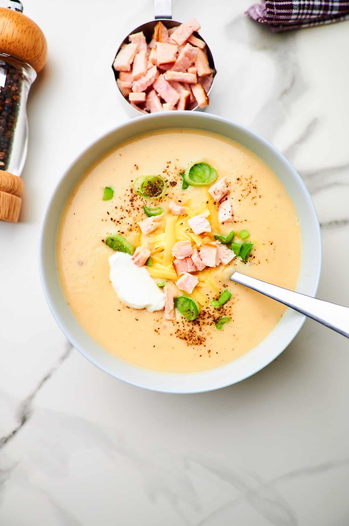 Overhead picture of potato soup that is made with mashed potatoes. The bowl of soup is topped with smoked turkey, cheese, sour cream, and green onions.