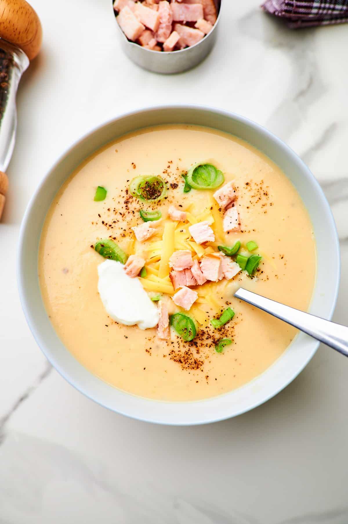 Overhead picture of potato soup that is made with mashed potatoes. The bowl of soup is topped with smoked turkey, cheese, sour cream, and green onions.