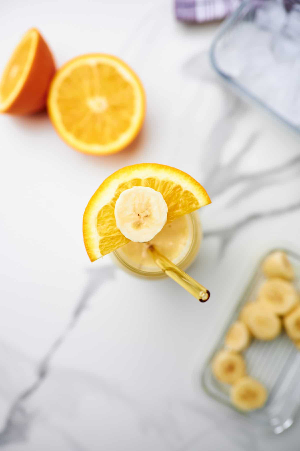 banana and orange banana smoothie in a glass with a glass straw