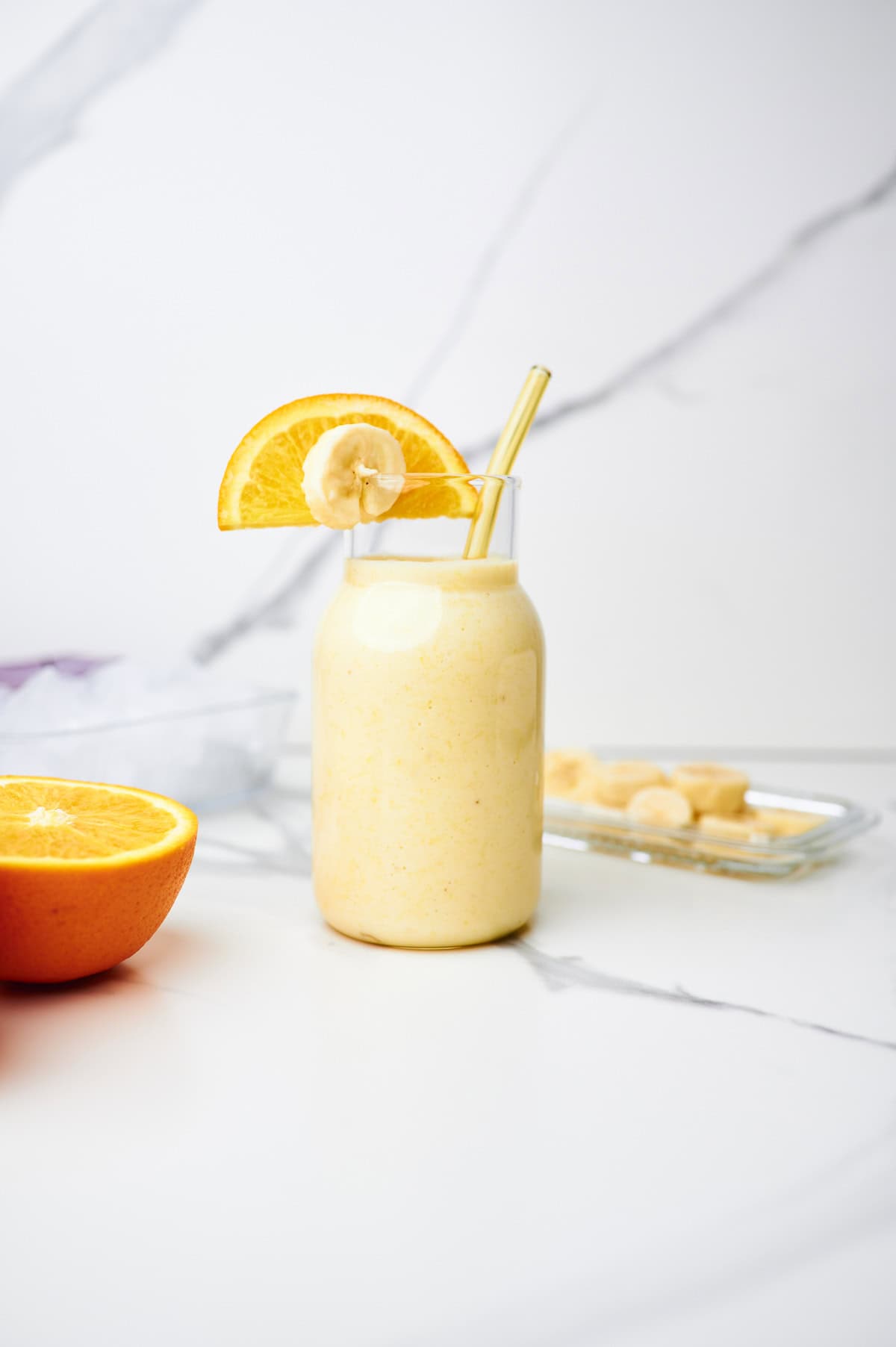 orange banana smoothie in a glass surrounded by banana and orange slices