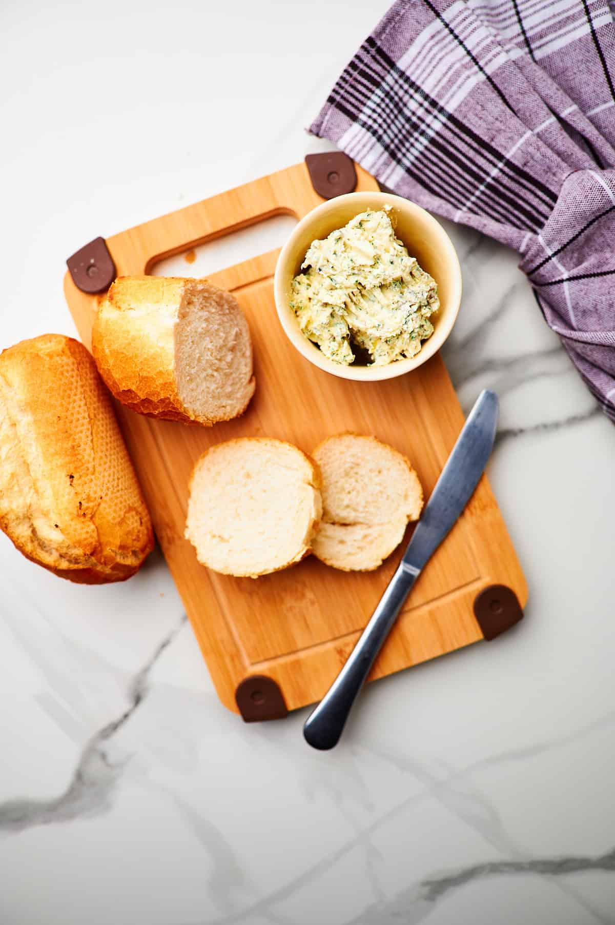 cutting board with garlic butter and sliced bread.