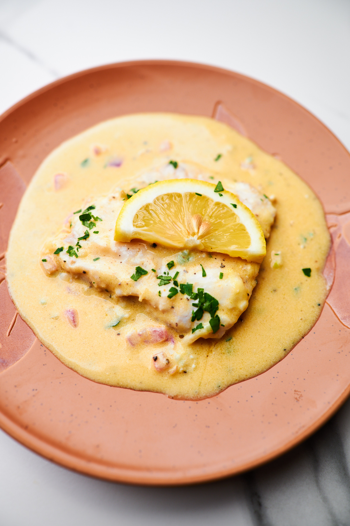 Close up photo of Baked Fish recipe with Lemon Cream Sauce in a white pan, fresh out of the oven