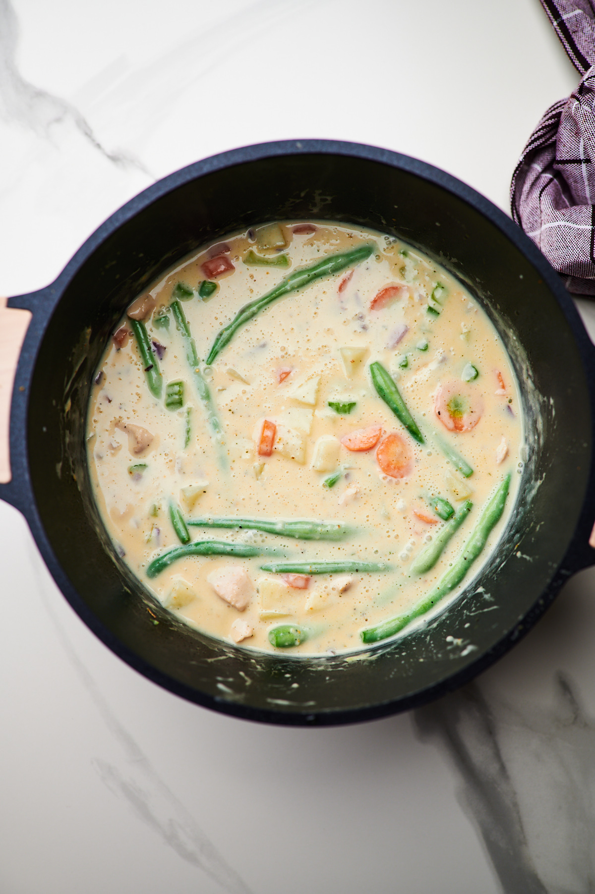 A soup pot filled with mixed vegetables and chicken next to the same pot topped with the creamy soup broth for creamy chicken stew.