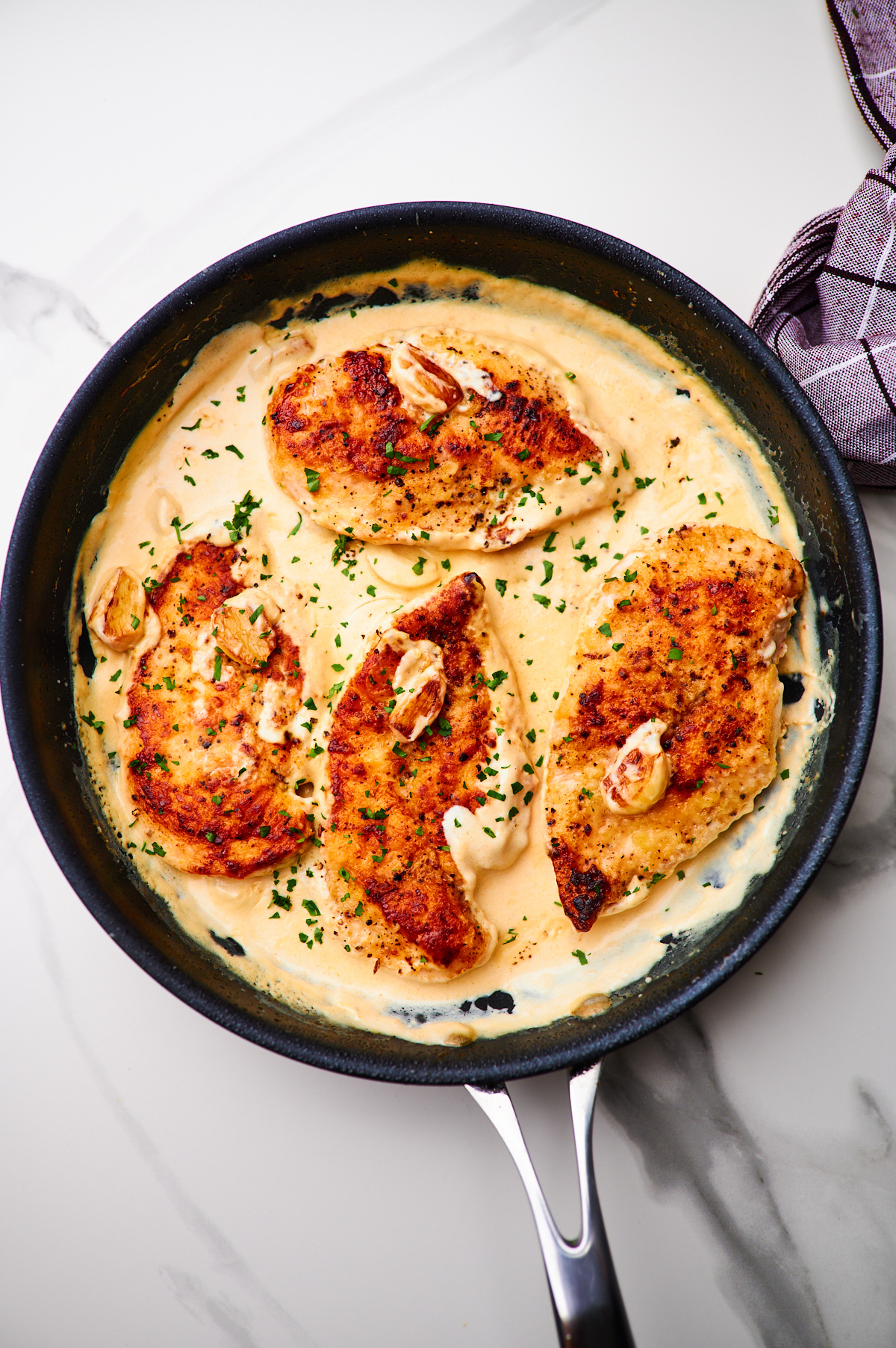 cast iron skillet with chicken breasts and a creamy garlic sauce with whole cloves of garlic